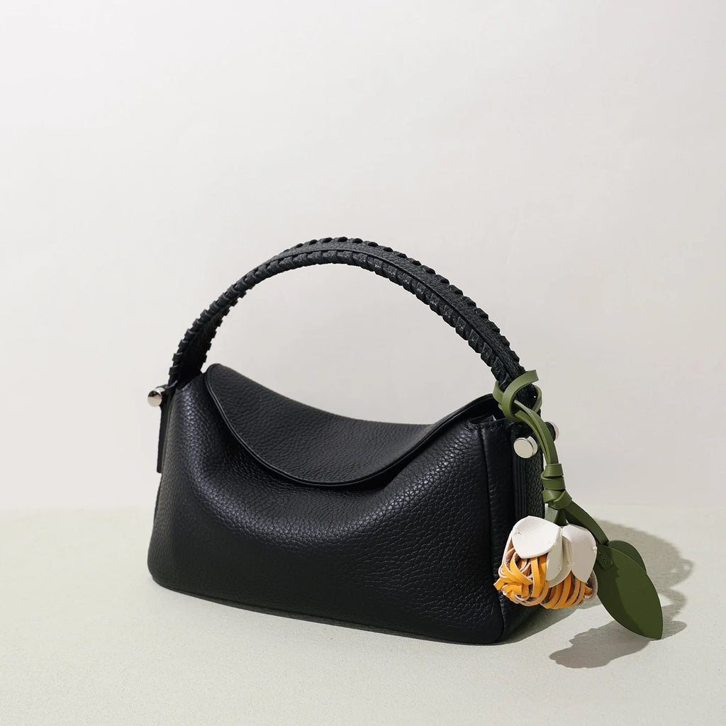 Small black pebble-grain leather designer handbag with braided top handle and flower-shaped decorative charm.
