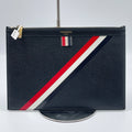 Black leather Thom Browne designer clutch with signature red, white, and blue diagonal stripe and gold zipper.