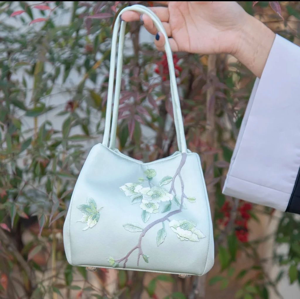 Mint green silk handbag featuring intricate white floral Su embroidery, slender shoulder straps, and a structured base.