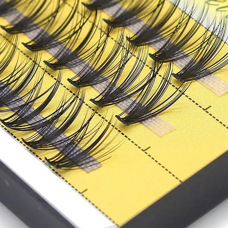 Black 20D mink Russian volume eyelash clusters arranged in rows on a bright yellow adhesive tray.