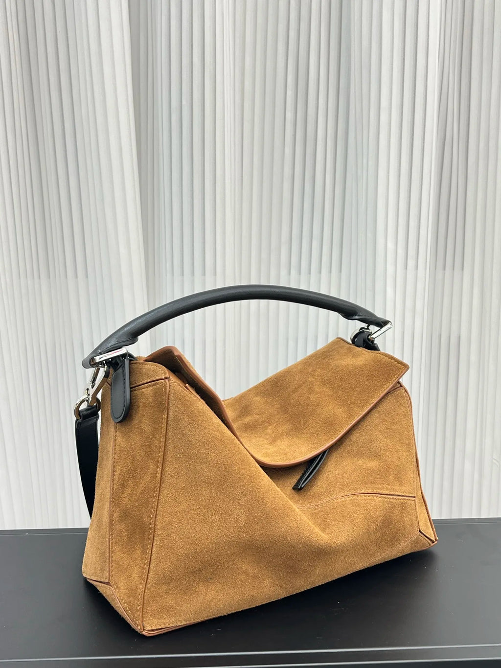 Tan suede designer crossbody handbag with black leather handle and unique geometric puzzle-inspired paneled design.