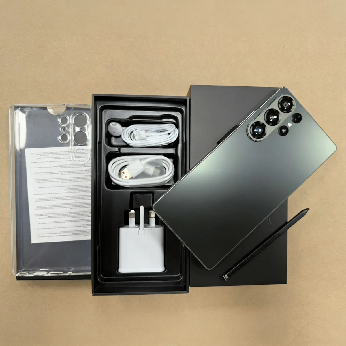 Dark green smartphone with quad rear cameras and open box accessories, cables and charger