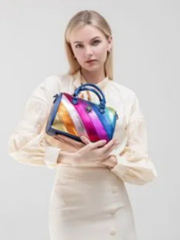 Kurt Geiger colorful metallic quilted trunk bag with eagle head logo and top handle held by woman in cream outfit.