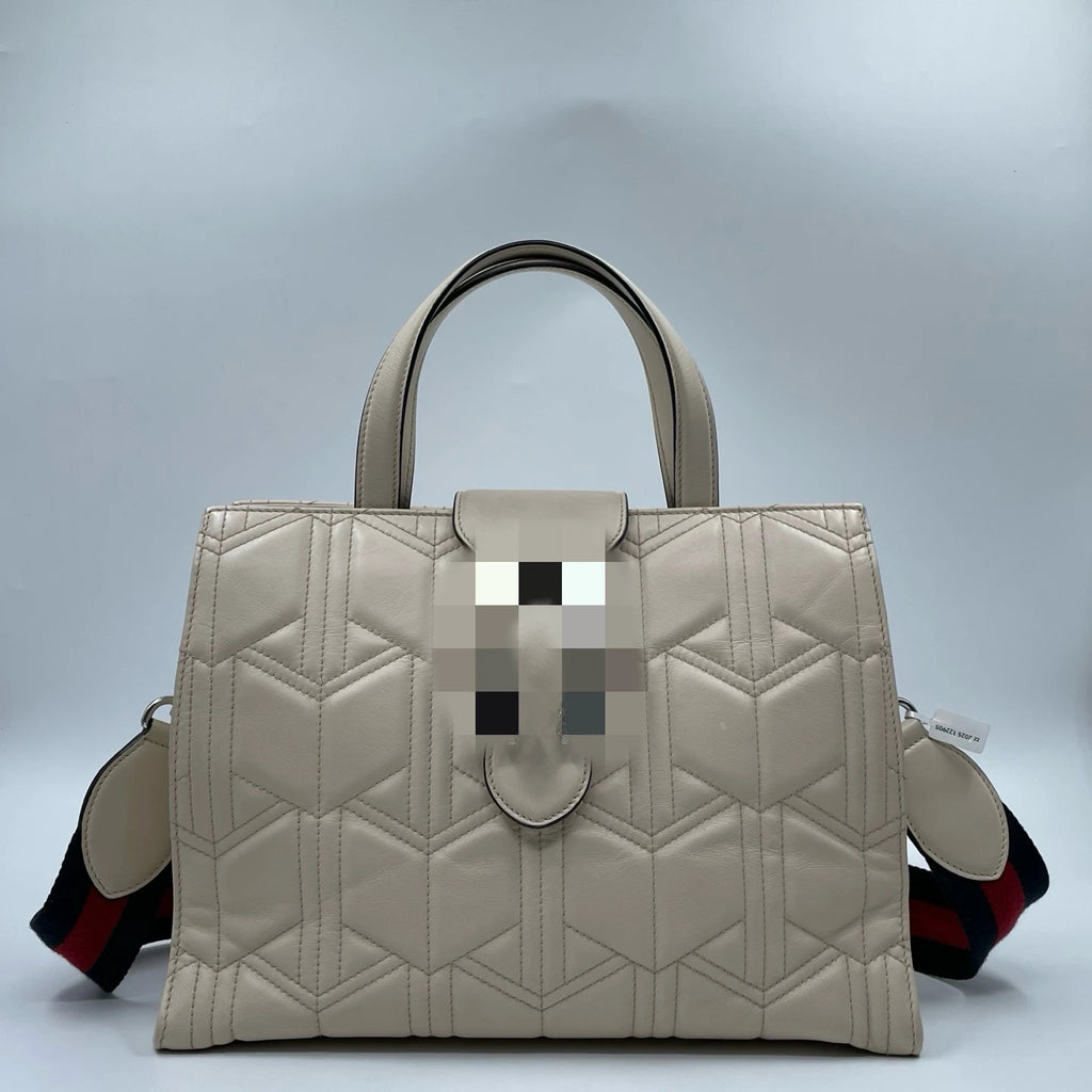 Elegant white quilted leather designer handbag with geometric stitching, dual handles, and striped shoulder strap.