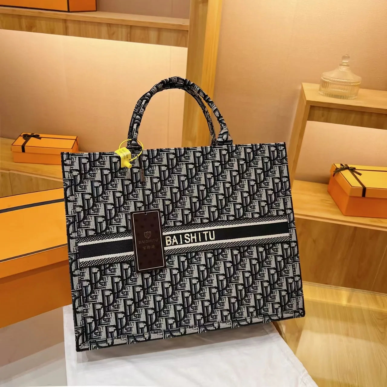 Black and white monogram canvas tote bag with top handles, Baishitu logo stripe, and structured trunk-style silhouette.