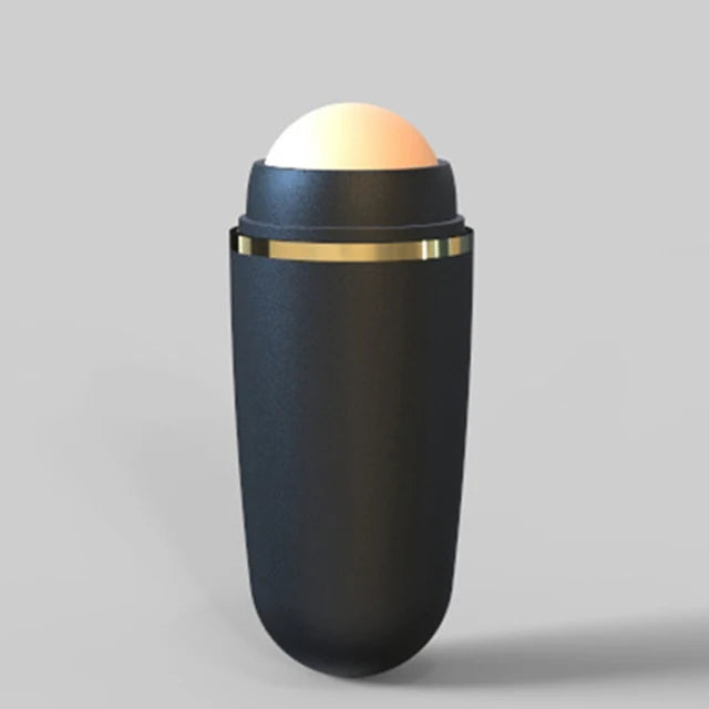 Matte black face oil absorbing roller with a pale, round volcanic stone tip and a thin gold band detail.