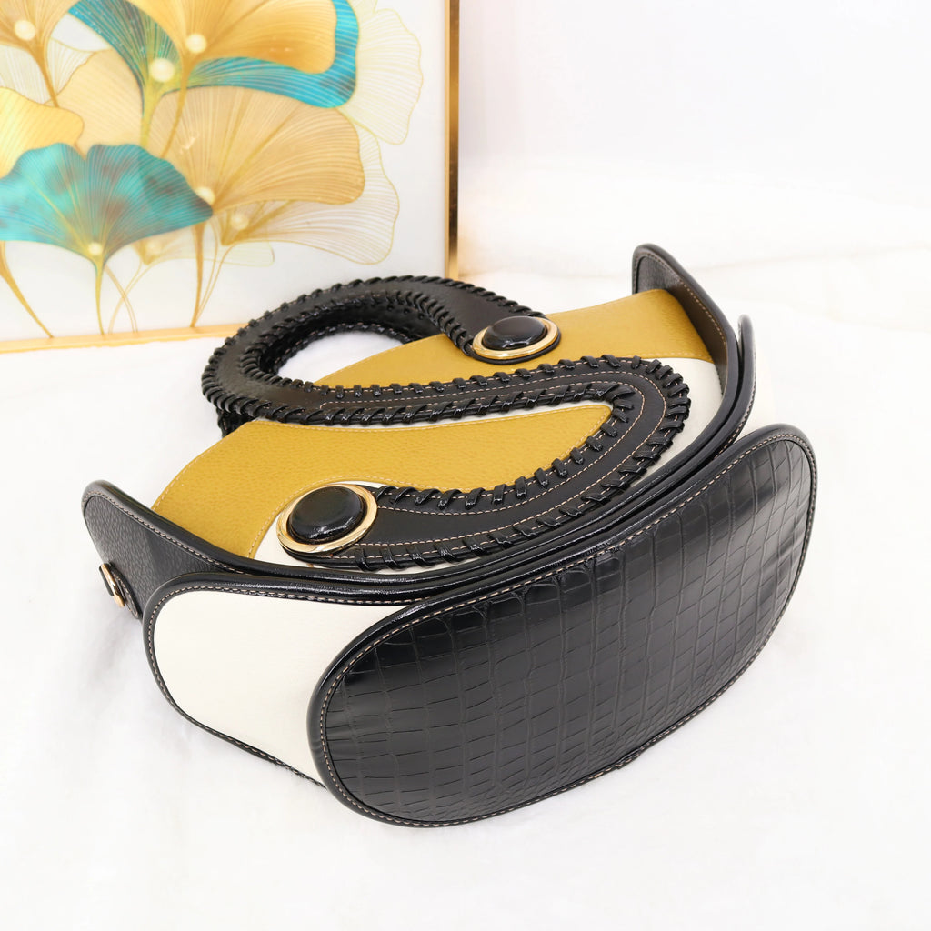 Designer handbag in black crocodile-texture and mustard leather with braided handles and unique circular hardware.