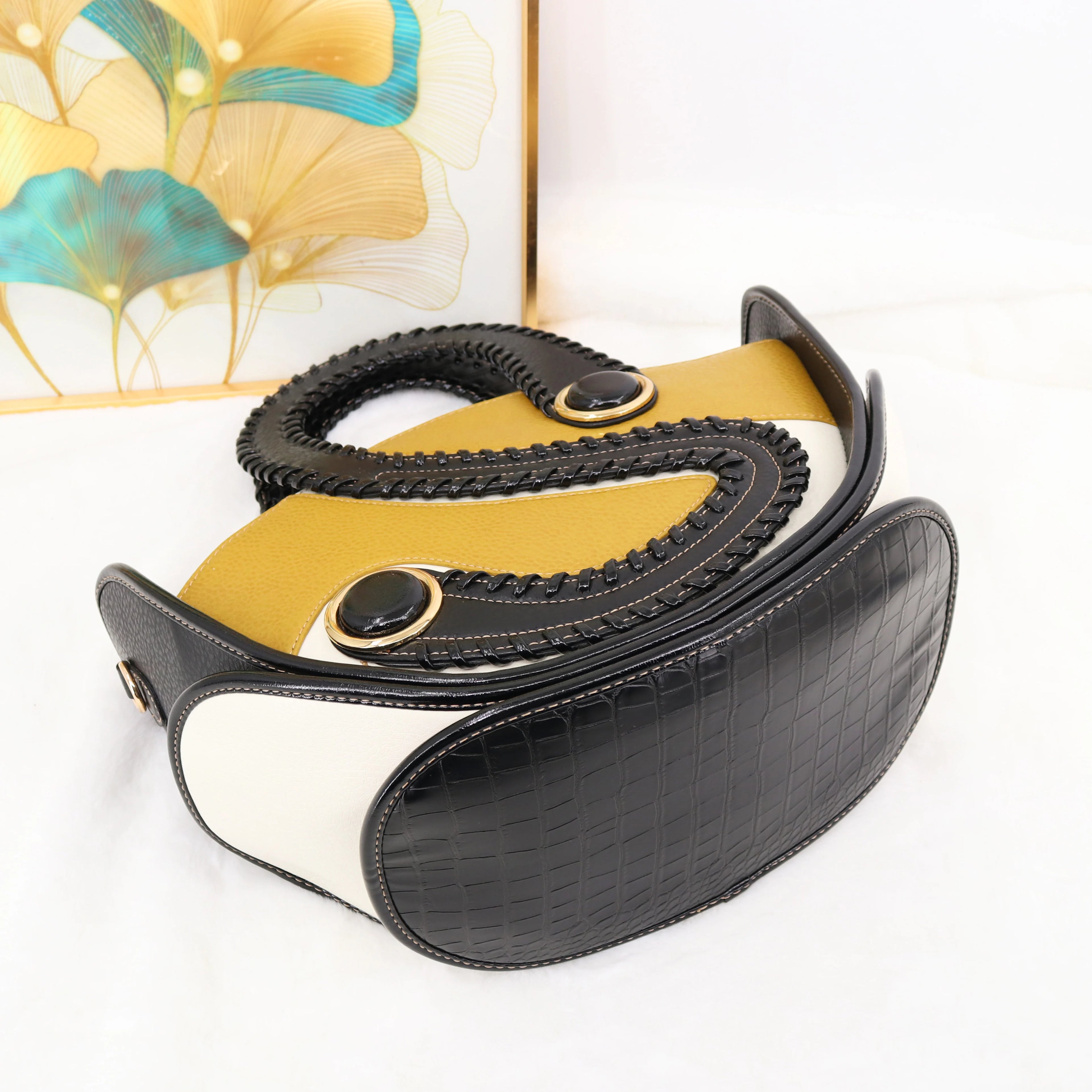 Designer handbag in black crocodile-texture and mustard leather with braided handles and unique circular hardware.