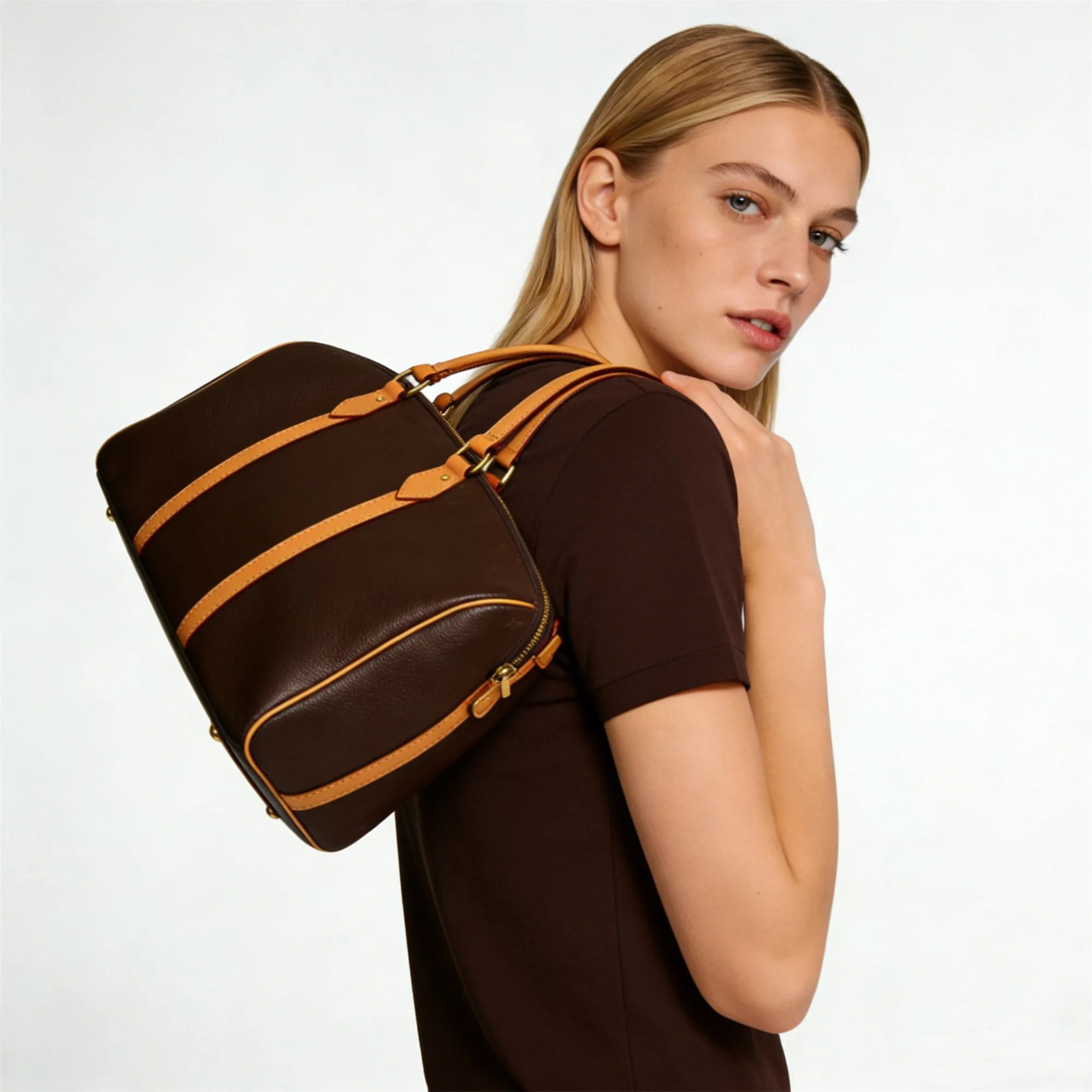 Brown leather trunk-style handbag with tan strap accents, gold hardware, and zipper closure worn on shoulder.