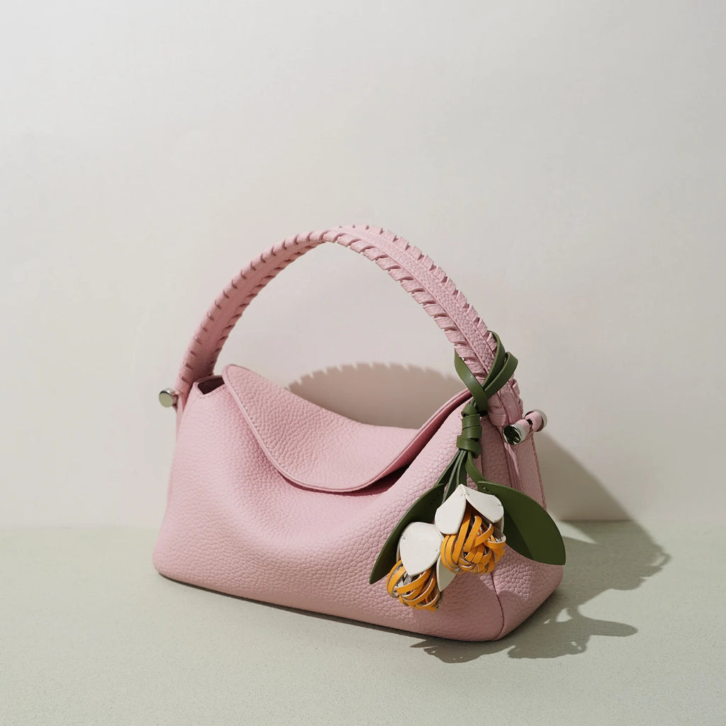 Pink genuine leather crossbody bag with woven top handle and decorative flower charm, designer small tote purse.