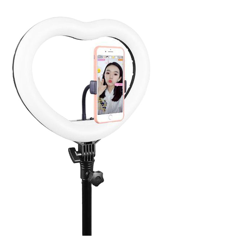 Heart-shaped white LED ring light on a black adjustable stand, holding a smartphone for photography and live streaming.