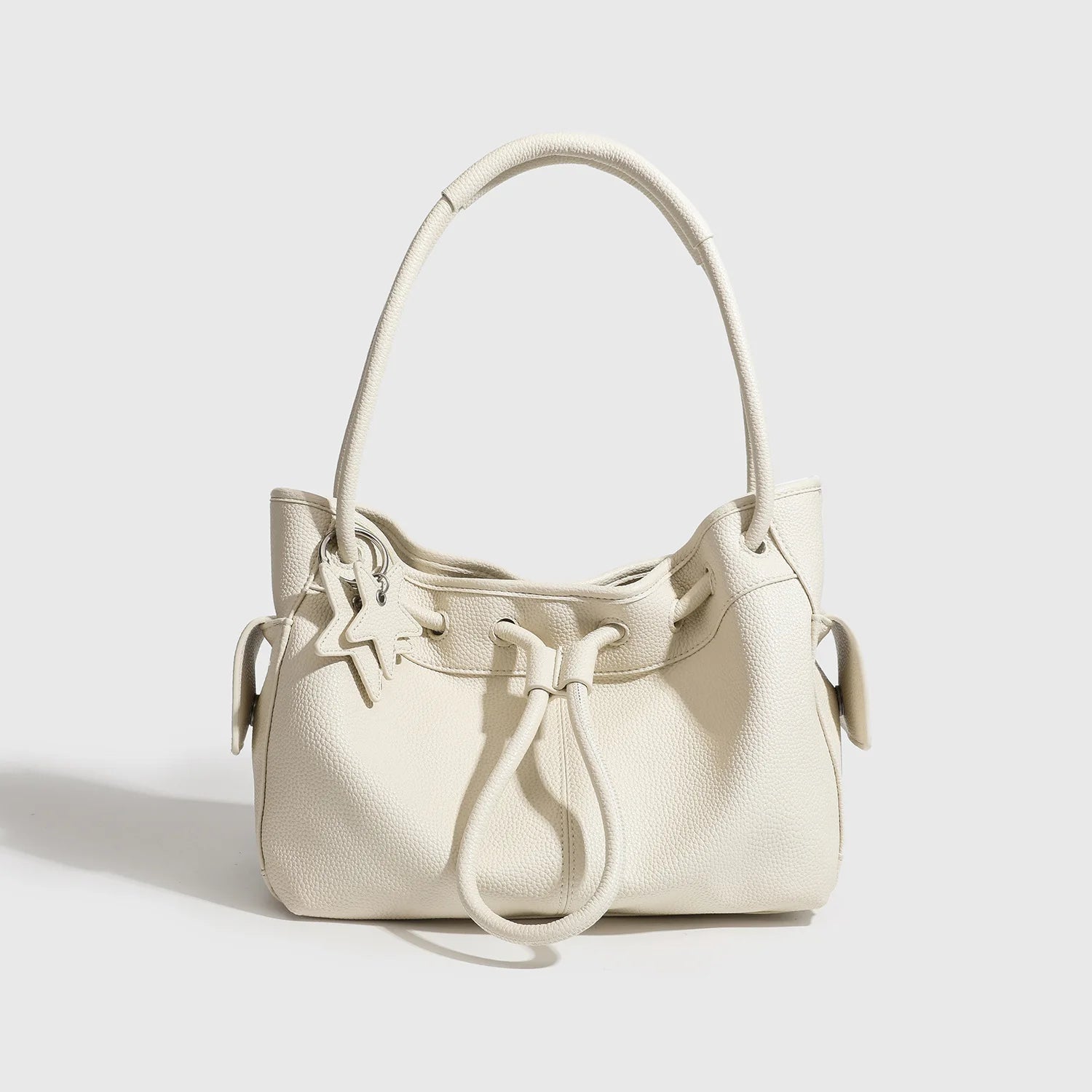 Off-white pebble-grain leather shoulder bag with drawstring closure, dual straps, and star charm. Minimalist aesthetic.