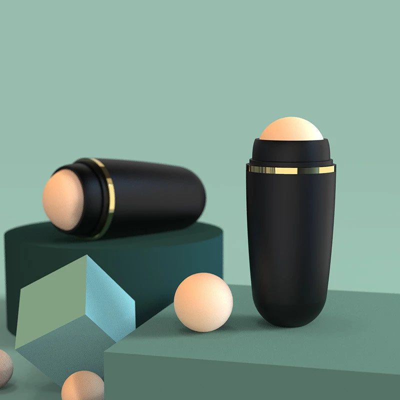 Two matte black volcanic stone face oil rollers with gold accents displayed on geometric platforms in sage green.
