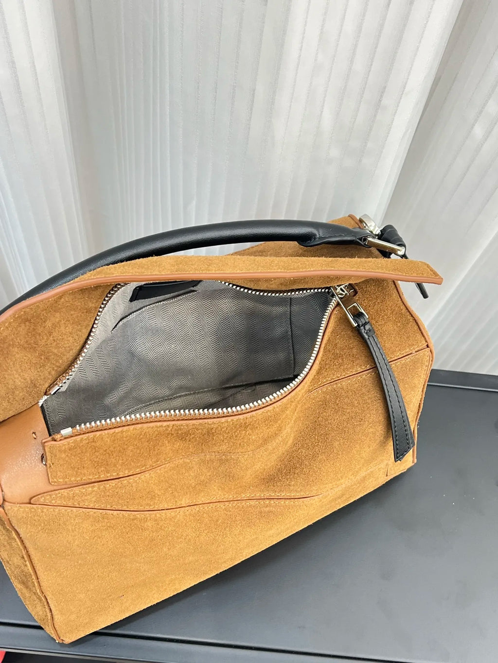 Tan suede designer crossbody handbag with black leather handle, zipper closure, and grey chevron-lined interior.