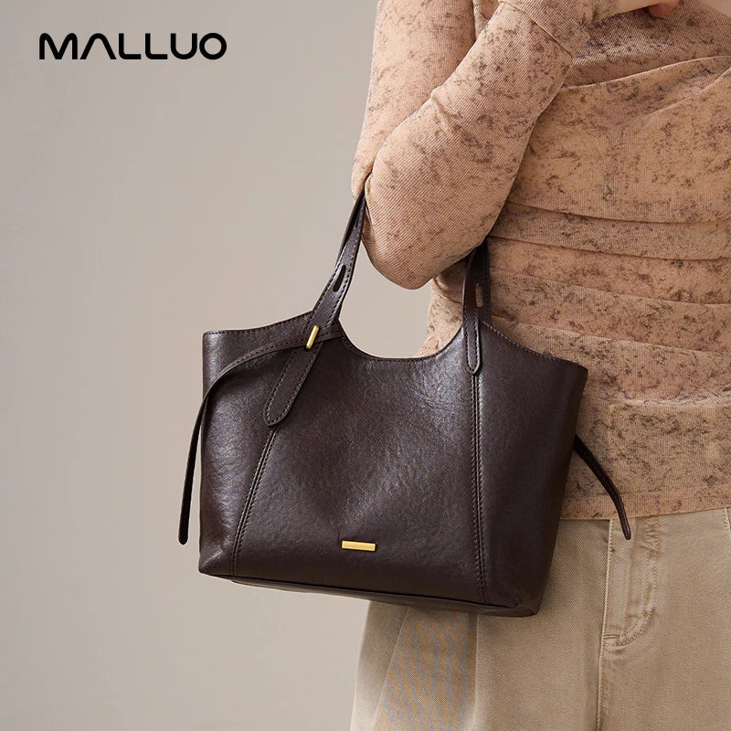 Dark brown top-grain leather designer armpit bag for women with gold hardware and minimalist tote silhouette.