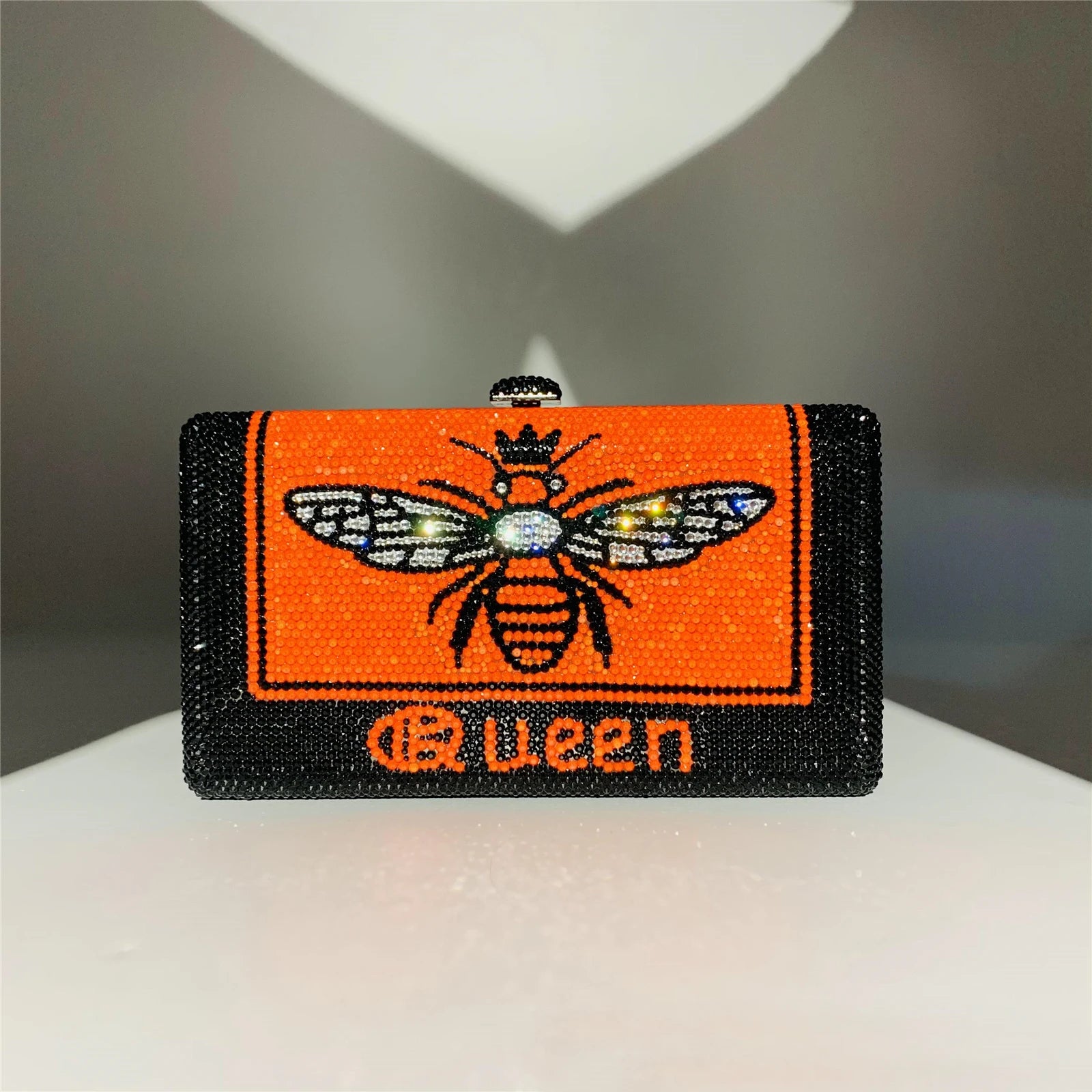 Black and orange rhinestone hard shell evening clutch with bee graphic and "Queen" text. Designer handbag style.