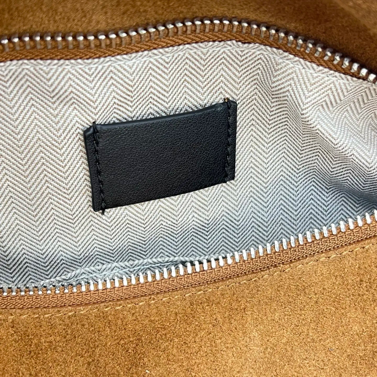 Tan suede designer handbag interior with silver zipper, chevron pattern lining, and blank black leather brand tag.