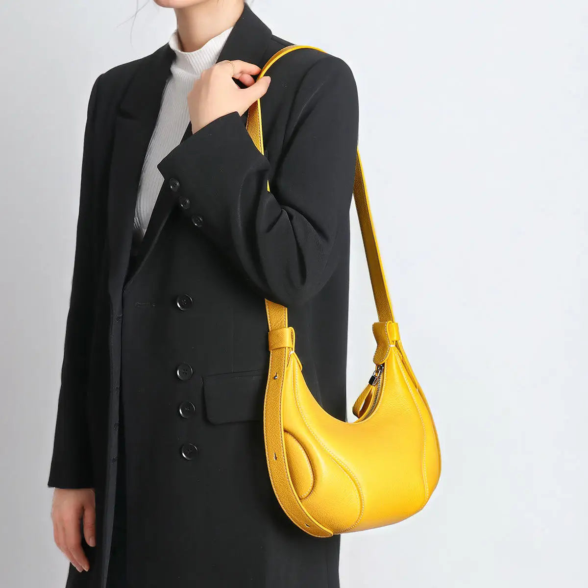 Yellow crescent-shaped leather crossbody handbag with structured trim, worn as an elegant shoulder trunk bag.