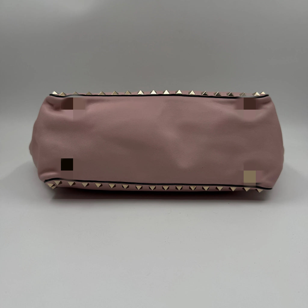 Pale pink genuine leather designer handbag featuring gold stud rivet detailing along the top and bottom edges.