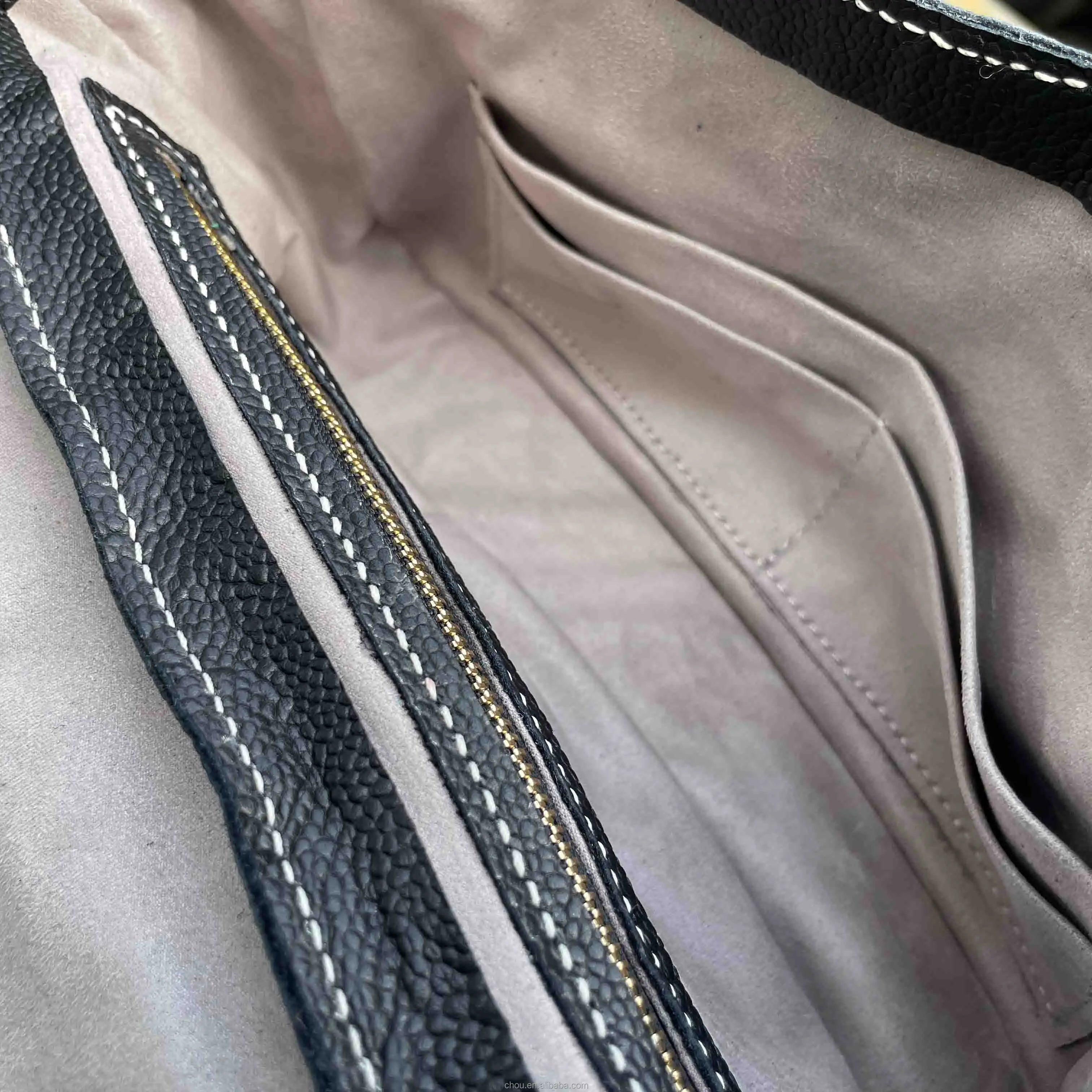 Interior of black pebbled calf leather luxury shoulder bag with beige suede lining, gold zipper, and slip pockets.