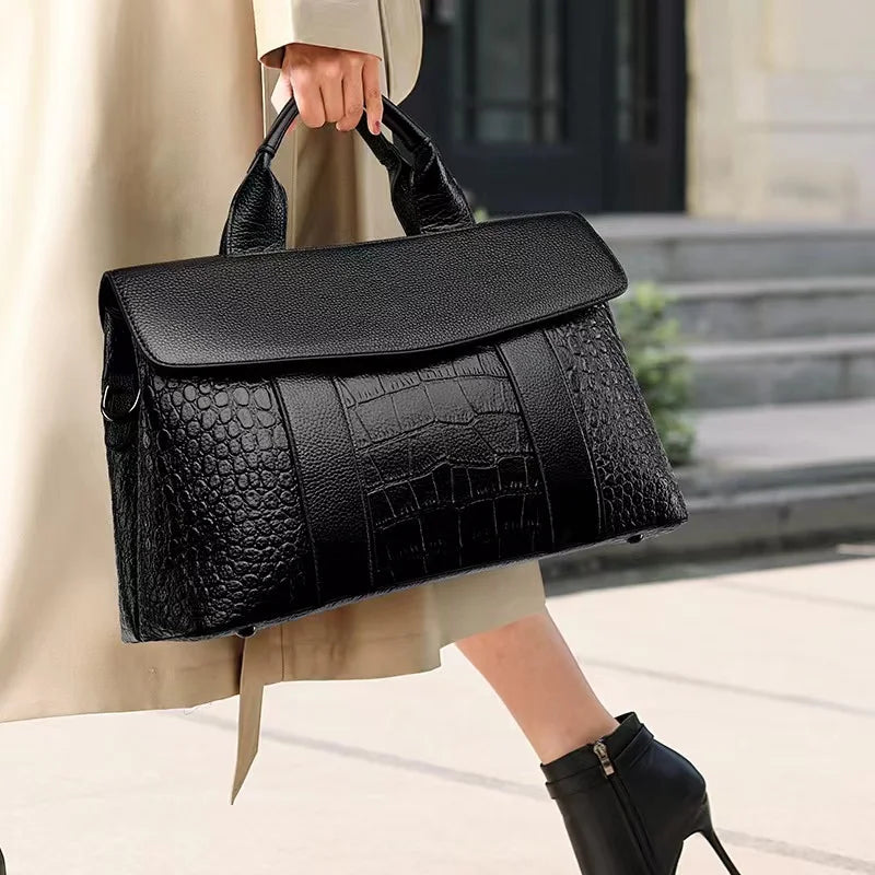 Black genuine leather designer handbag with crocodile-embossed texture and flap closure, held by a woman in a trench.