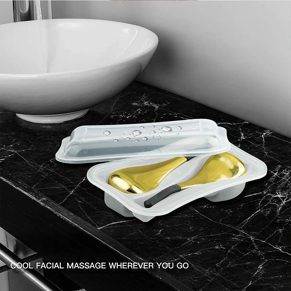 Two gold cooling facial massage globes with black handles resting in a clear plastic carrying case on a marble counter.