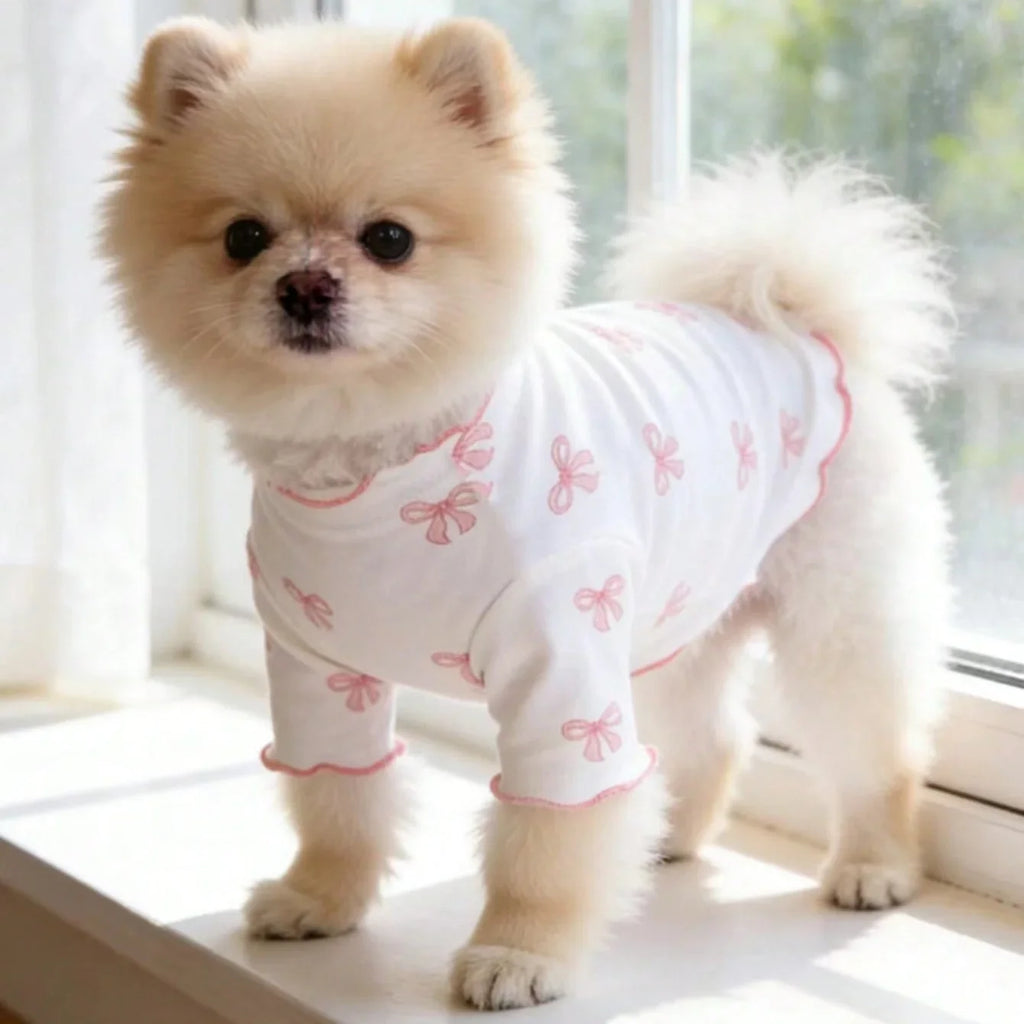 Cute Pomeranian wearing a breathable white knit dog shirt with pink bow tie print for comfortable, stretchy pet fashion.