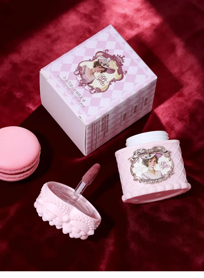 Vintage matte velvet lip mud with soft focus finish in a pink ornate jar with applicator on a red velvet background.