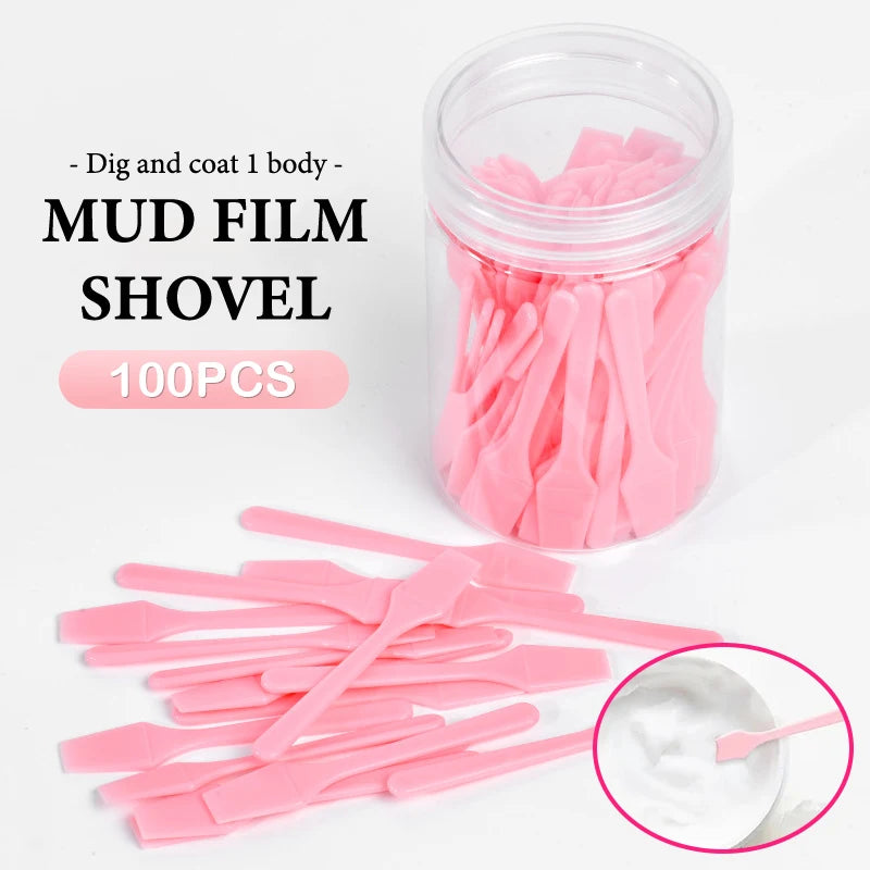 A set of 100 small, pink plastic cosmetic spatulas in a clear jar, with several loose on the table.