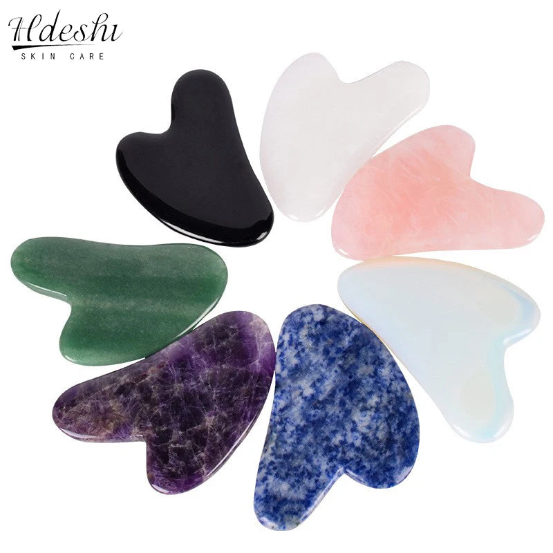 Seven heart-shaped Gua Sha facial massage tools made of various polished stones in a circular arrangement.