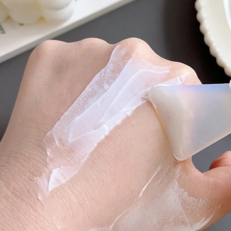 A translucent, flexible silicone spatula applying a smooth white face mask cream onto a person's hand.