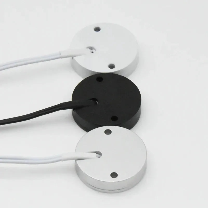 Recessed puck lights in white, black, and silver with mounting holes and cords