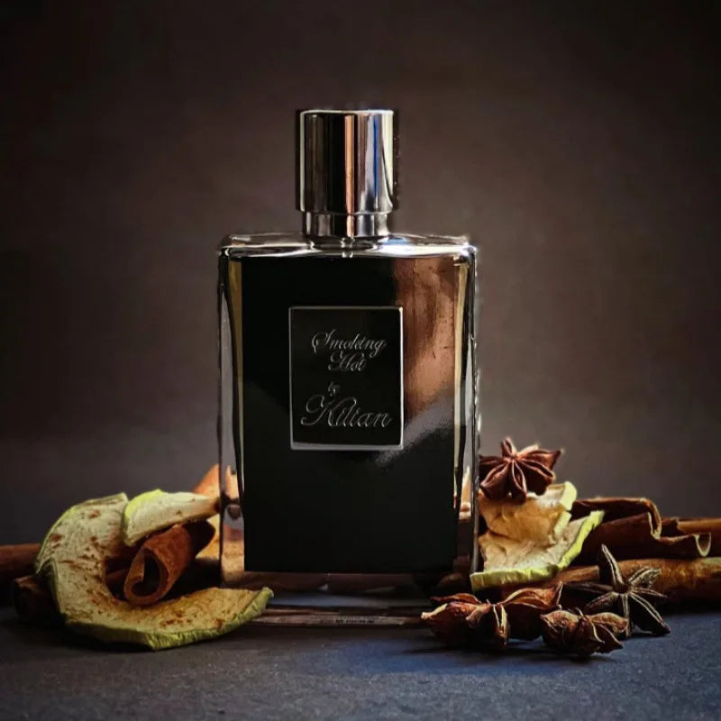 Kilian Smoking Hot 50ml perfume bottle with a glossy black finish, surrounded by cinnamon sticks and star anise spices.