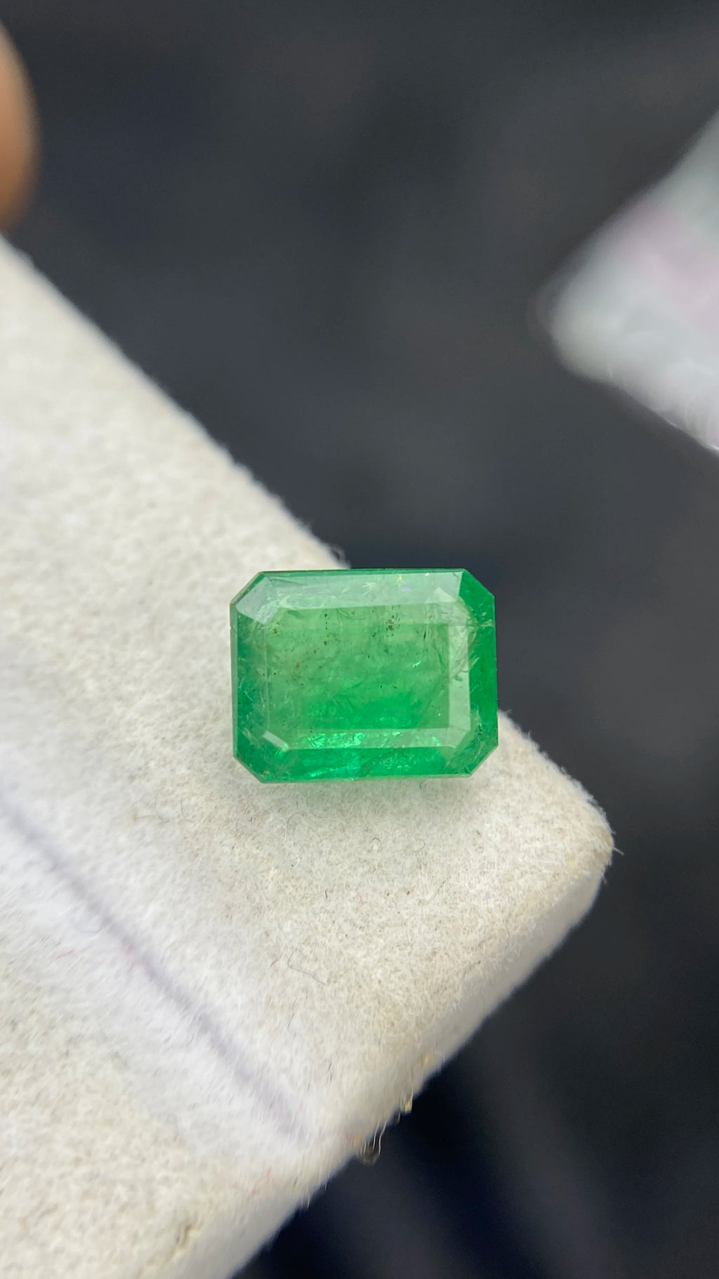 Small green emerald-cut gemstone, loose stone on light display pad