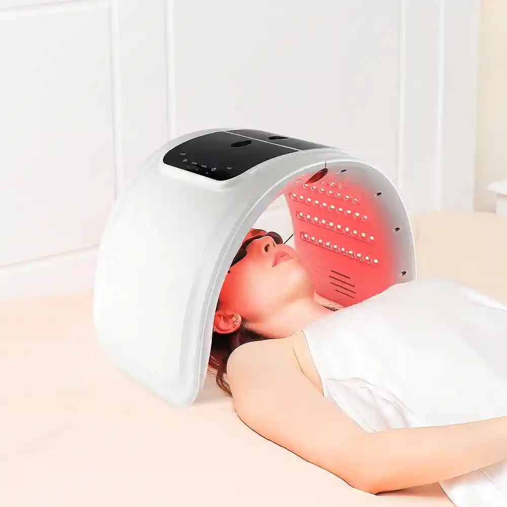 Woman lying on a bed using an arched white LED light therapy machine over her face with red light panels.