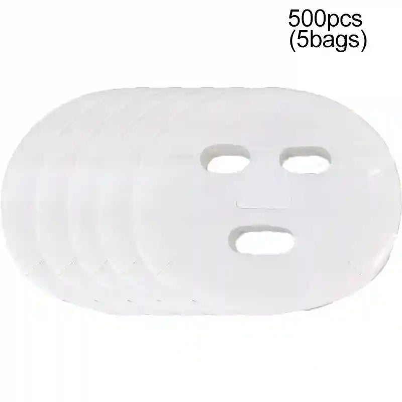 A stack of five thin, white, disposable facial mask sheets with cutouts for eyes, nose, and mouth.