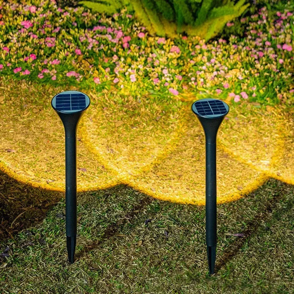 Two black solar stake lights illuminate a garden lawn, casting warm glowing light pools on the ground.