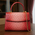 Red ostrich-embossed genuine leather designer handbag with a top handle and gold chain shoulder strap.