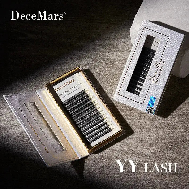 Two boxes of black DeceMars YY-shaped volume eyelash extensions in white, diamond-textured packaging on stone surface.