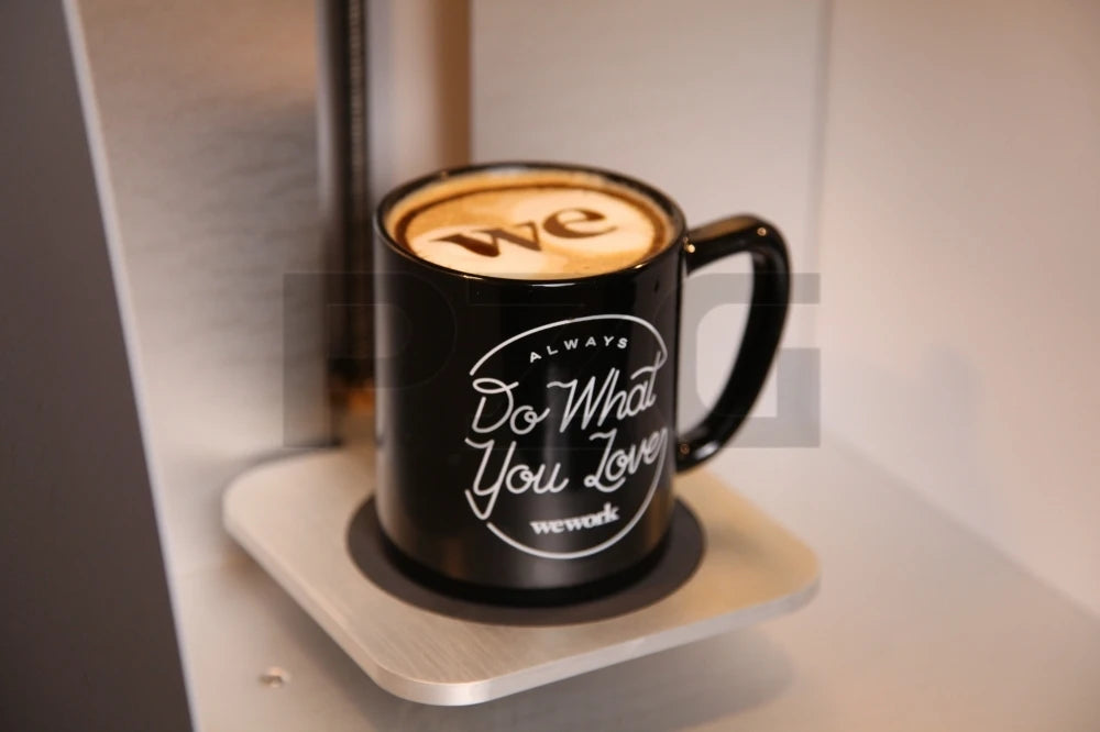 Black WeWork ceramic coffee mug with Do What You Love logo sitting on a modern automatic coffee machine base.