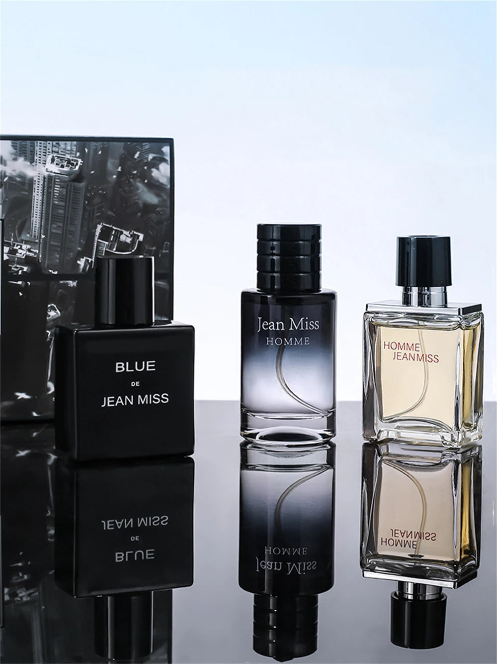 Three Jean Miss men's fragrance bottles on a reflective surface: one matte black, one grey gradient, one clear glass.