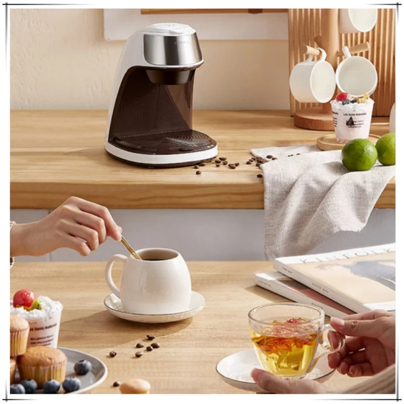 KONKA compact white and chrome single-serve coffee maker on a kitchen counter with coffee beans and tea cups.