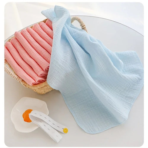 Soft muslin baby care washcloths in pink and blue, neatly stacked in a wicker basket with an accessory.
