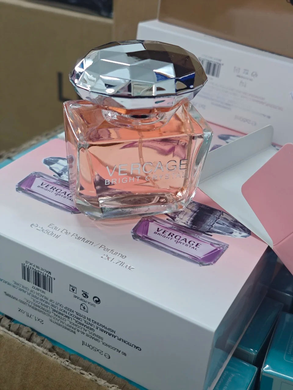 Glass bottle of Vercage floral perfume with pink liquid and a silver faceted cap, sitting on a branded display box.