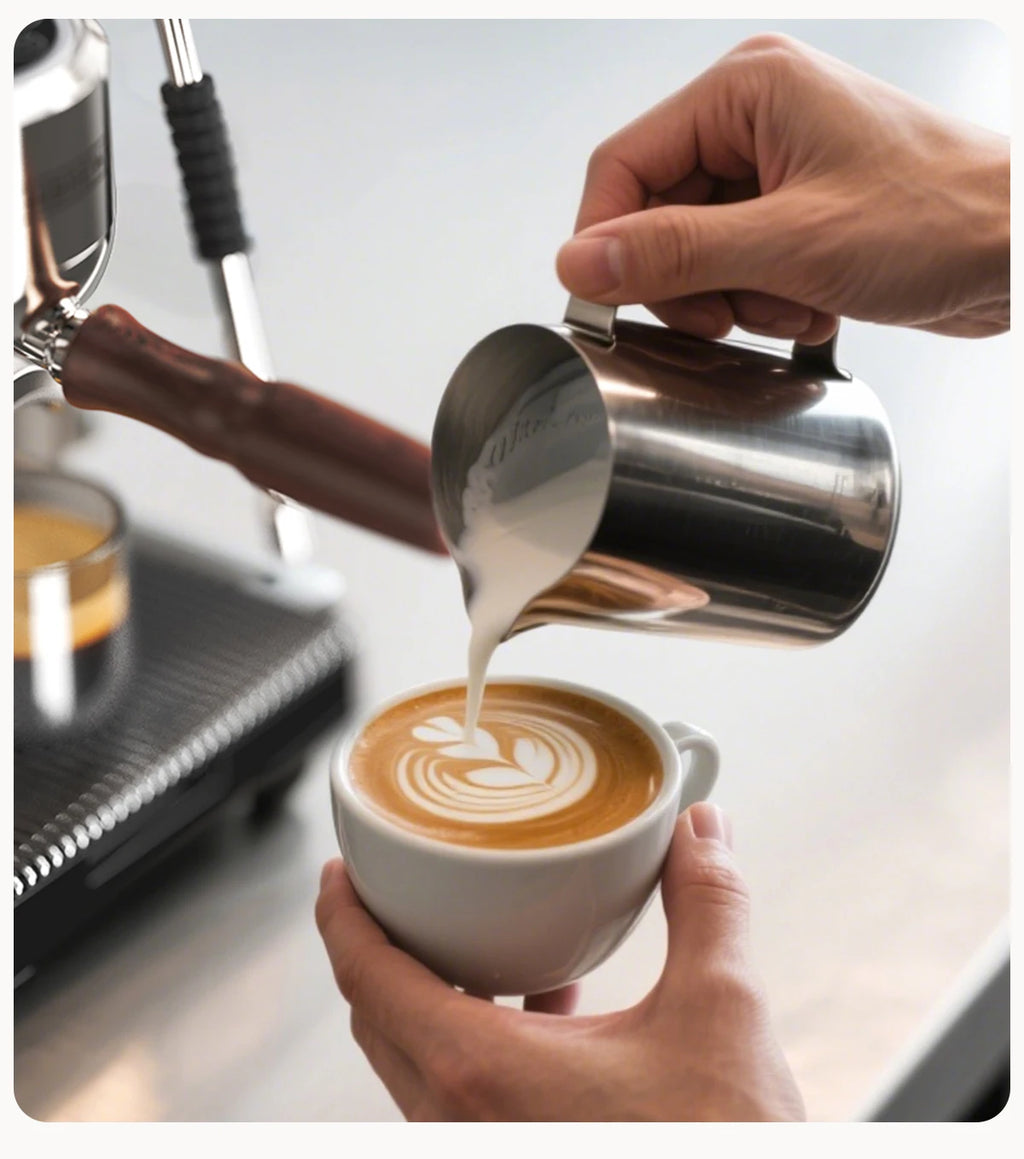 Stainless steel milk frothing pitcher pouring latte art from an espresso machine with wooden handle portafilter.