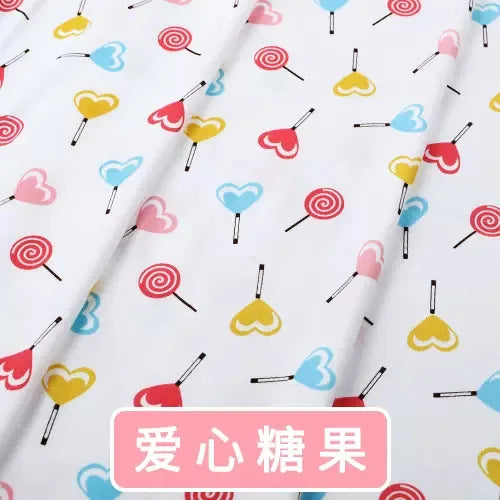 White knit jersey fabric with a colorful print of heart-shaped lollipops and swirls for children's clothing.