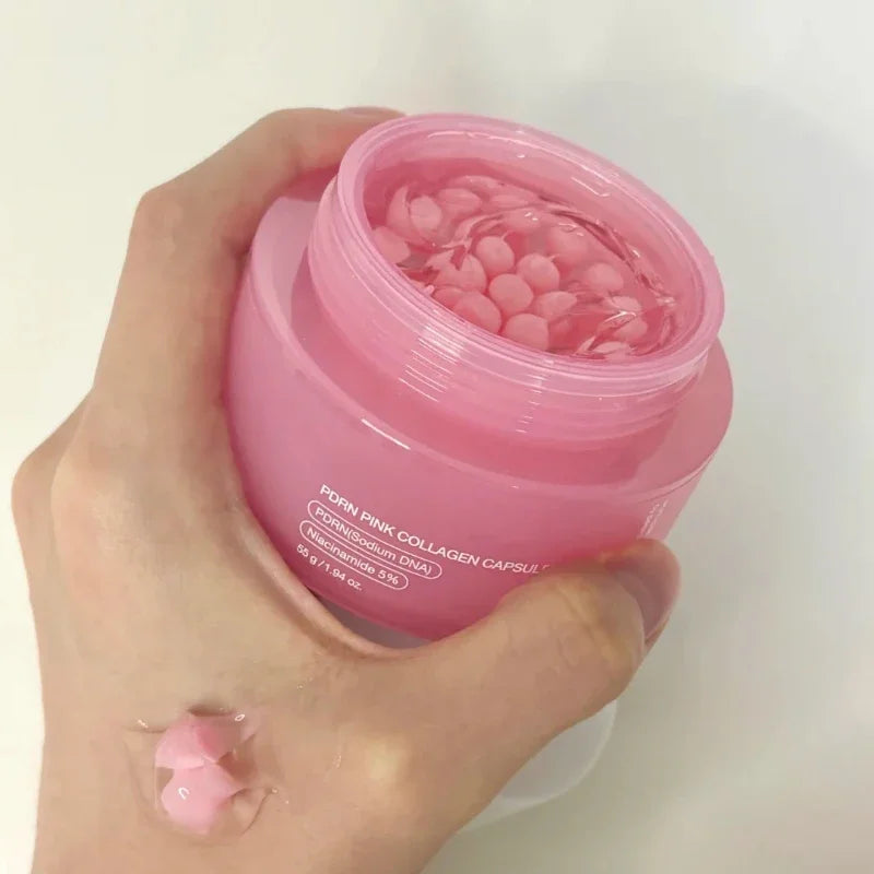 A hand holding an open pink jar of collagen capsule cream, with a small amount of the pink product swatched on skin.