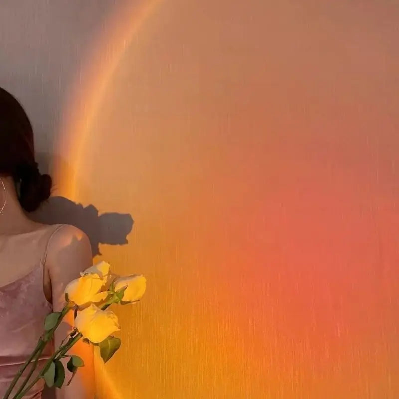 Sunset lamp projecting a large, circular orange and yellow gradient light on a wall, illuminating a person holding