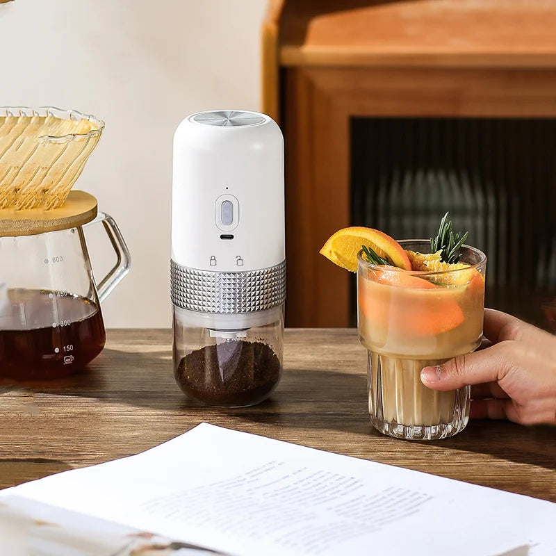 White portable electric coffee grinder with metallic textured grip and clear grounds container on a wooden table.