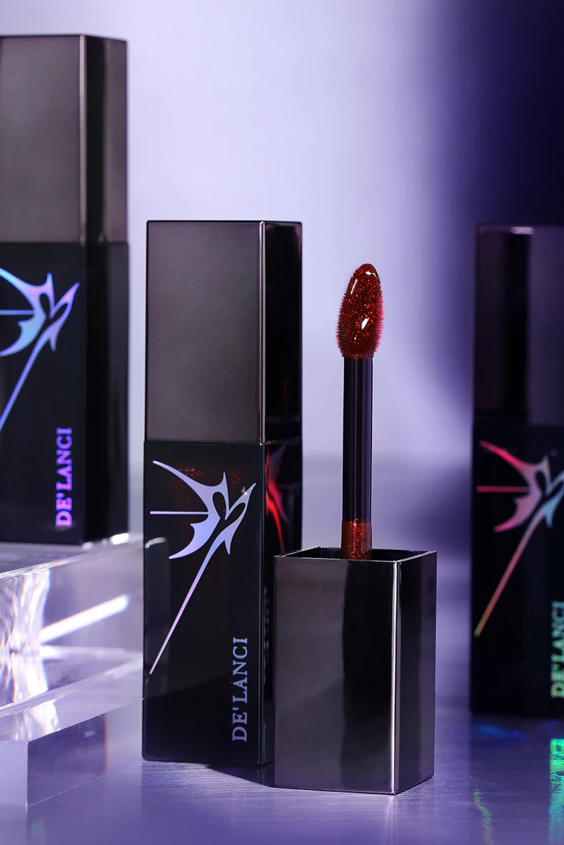 DE'LANCI gothic shimmer lip gloss with sparkly red applicator wand and sleek black tube packaging for smoky punk makeup.